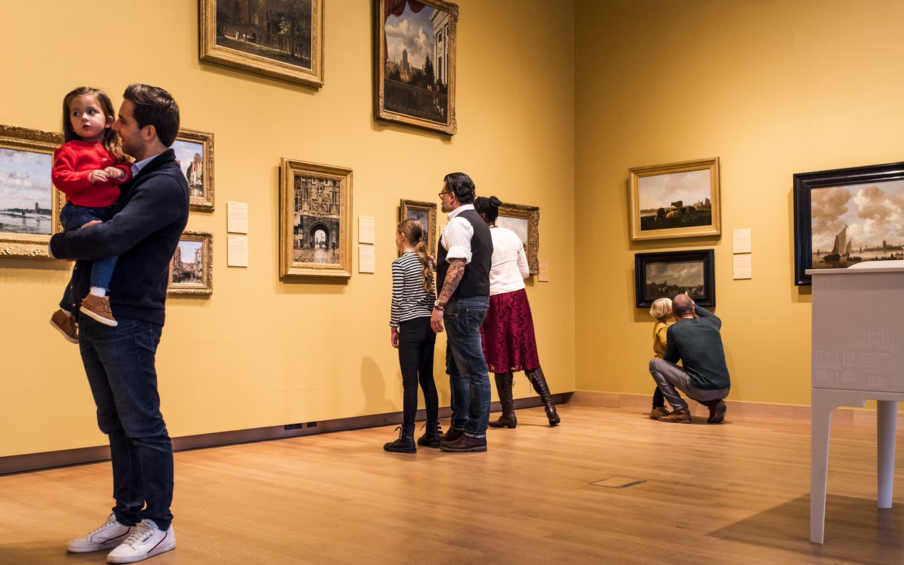 In een museumzaal staan mensen te kijken naar de schilderijen.