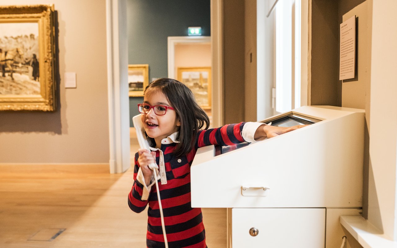 Een vrolijk meisje staat bij een interactief scherm in het Dordrechts Museum en luistert naar de uitleg.