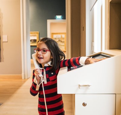 Een vrolijk meisje staat bij een interactief scherm in het Dordrechts Museum en luistert naar de uitleg.