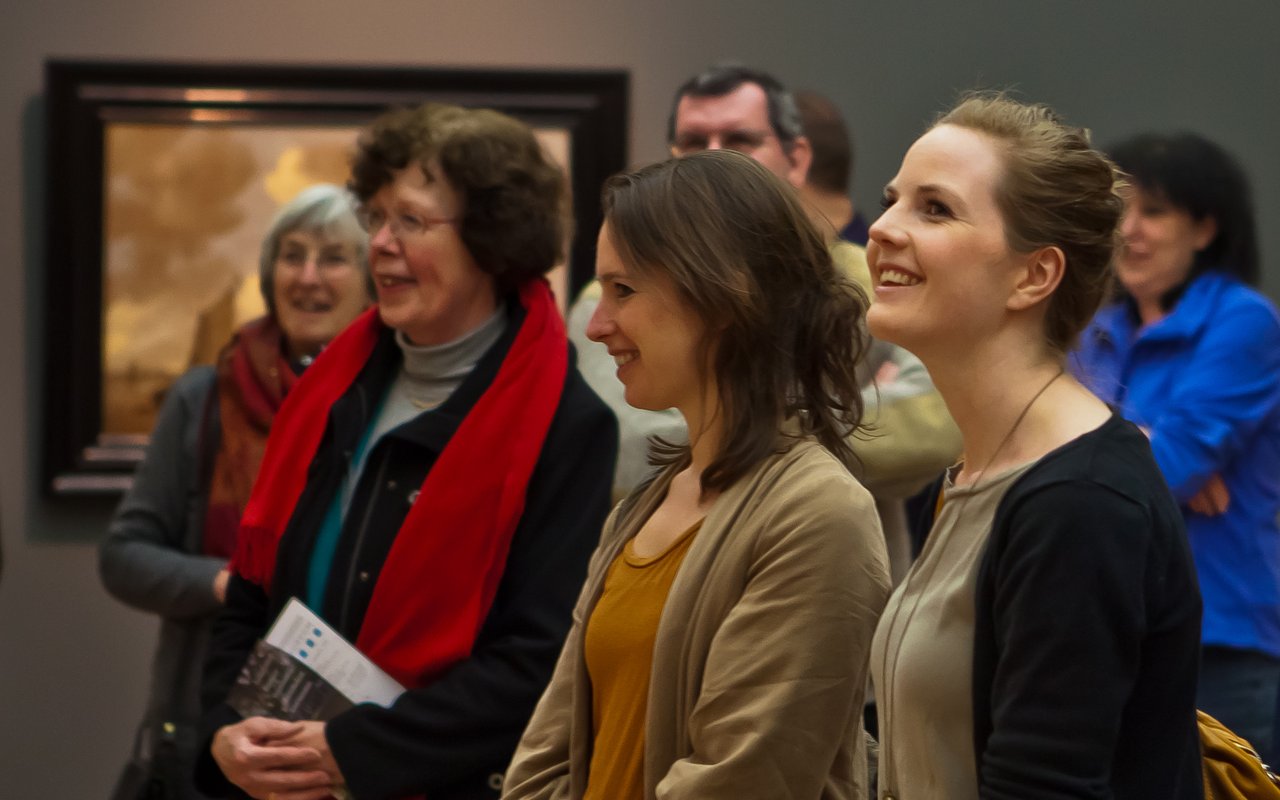 Twee lachende jonge vrouwen met daarachter een menigte, kijken naar een schilderij in Dordrechts Museum tijdens de Masterclass voor docenten.