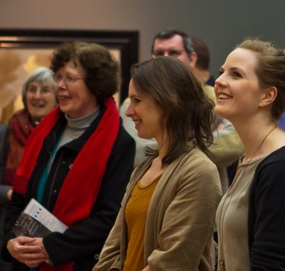 Twee lachende jonge vrouwen met daarachter een menigte, kijken naar een schilderij in Dordrechts Museum tijdens de Masterclass voor docenten.