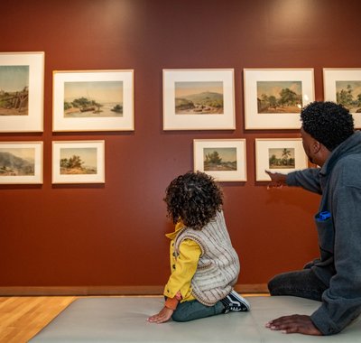 Man en kindje op een bankje in het museum. De man wijst naar een kunstwerk.