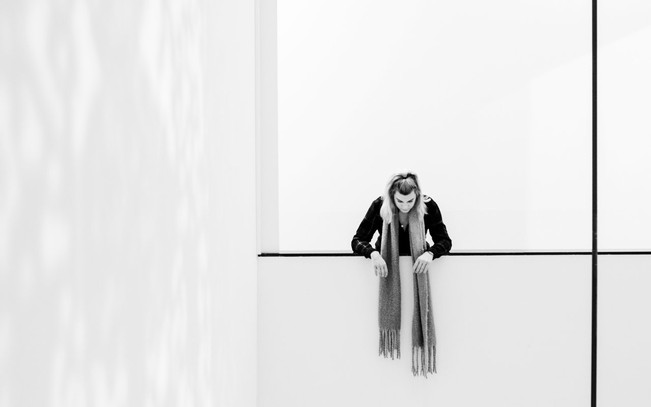 Vrouw met lange sjaal kijkt vanaf de balustrade naar beneden.