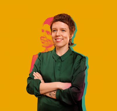 De kunstenaar Tasha Arlova staat lachend voor een gele achtergrond. Ze doet mee aan de Galatea Kunstprijs 2023 in het Dordrechts Museum.