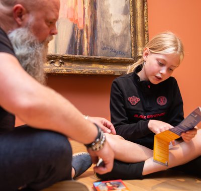 Een vader en zijn dochter lezen samen de instructie van het Museumdobbelspel.