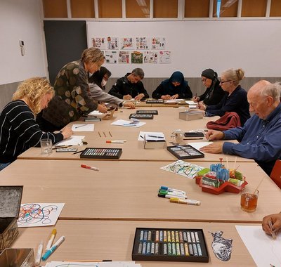 Workshop 'Cuyp op de koffie' waarbij mensen aan tafel tekenen. Op locatie van Buurtwerk Dordrecht bij Trefpunt de Nieuwe Stoof in Crabbehof.