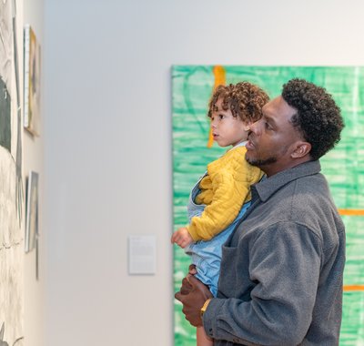 Man met kindje op de arm kijkt naar een schilderij