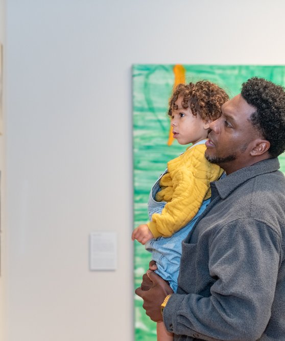 Man met kindje op de arm kijkt naar een schilderij