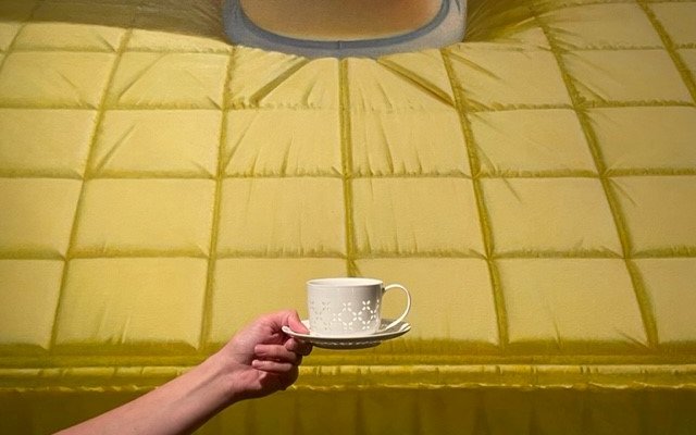Voor het kunstwerk BED van Jan Beutener, houdt iemand een koffiekopje omhoog.