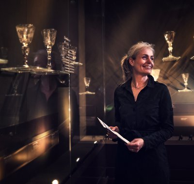 Lachende vrouw met folder in haar hand staat bij de glascollectie.