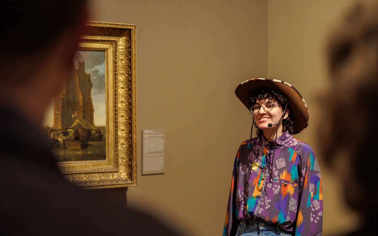 Een enthousiaste vrouw met een cowboyhoed leidt mensen rond door het museum.