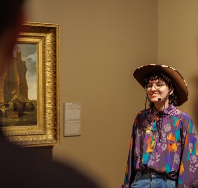 Cherylia van Take pART geeft een rondleiding in het Dordrechts Museum. Een enthousiaste vrouw met een cowboyhoed leidt mensen rond door het museum.