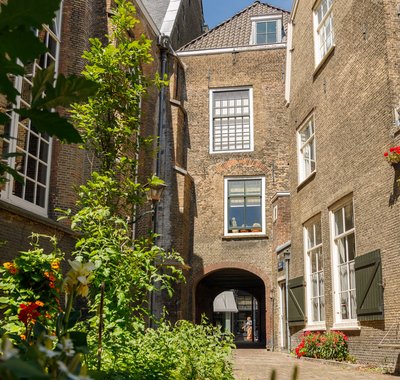 Steegje tussen de Augustijnenkerk en Hof van Nederland . Er groeien planten en bloemen in een perkje.